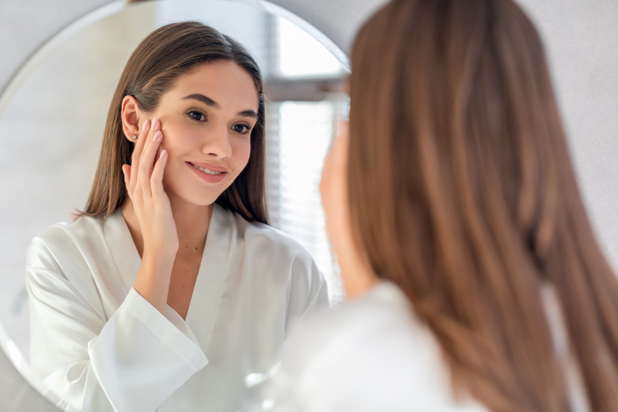 Portrait Of Attractive Young Female Smiling To Her Reflection In Mirror | AviClear® for Skin Rejuvenation 